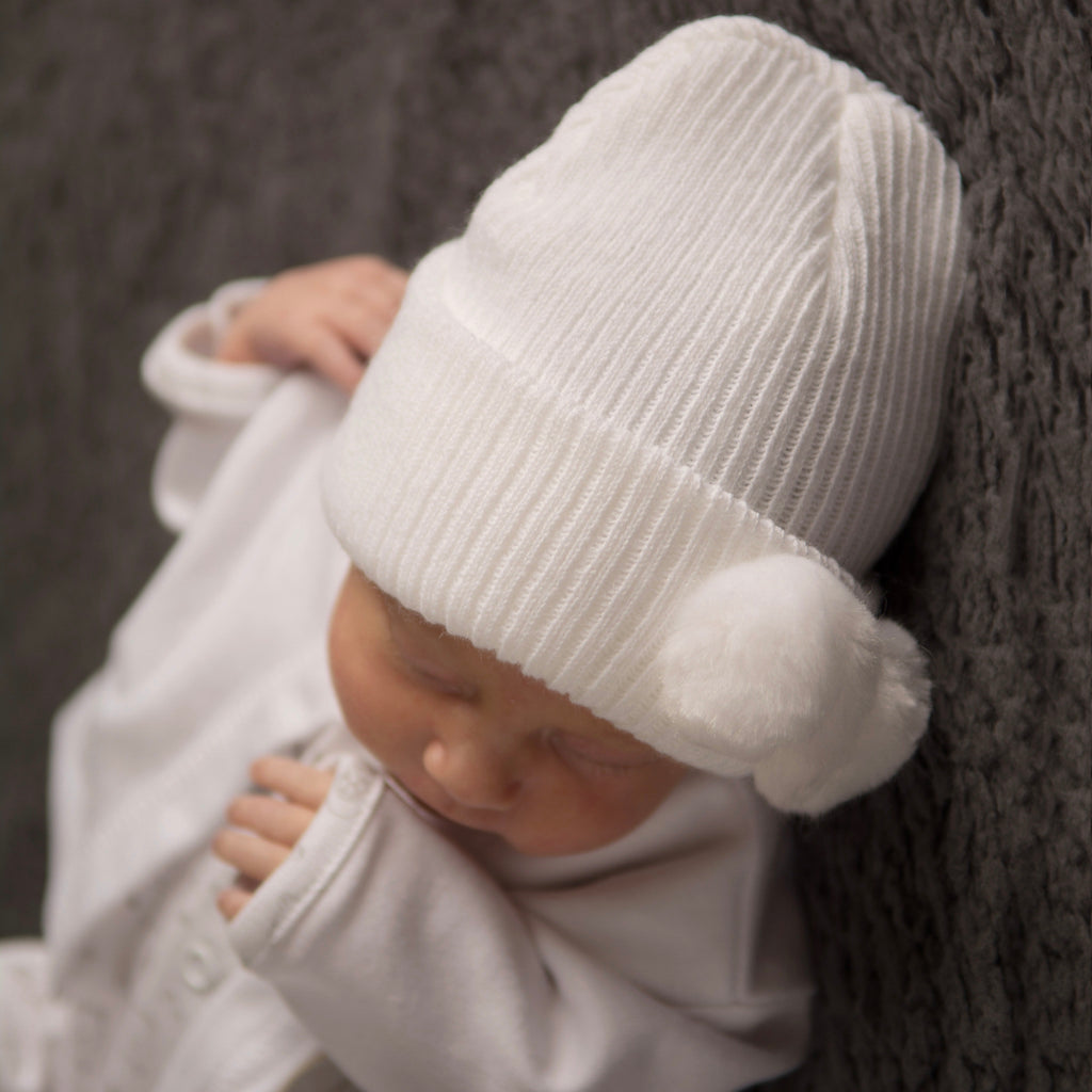 Baby wearing first size white hat with white pom pom