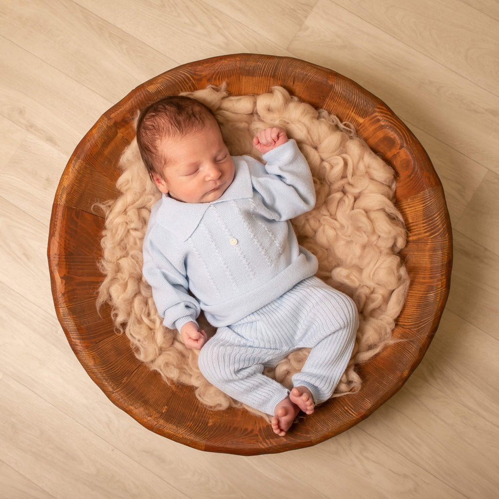 Baby in wooden bowl on fur blanket wearing blue polo knitted jumper and trousers set
