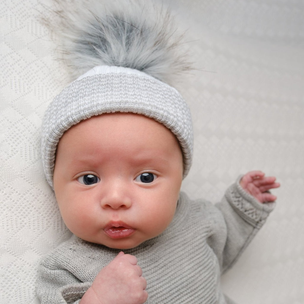 Baby wearing first size white and grey ribbed fur pom hat