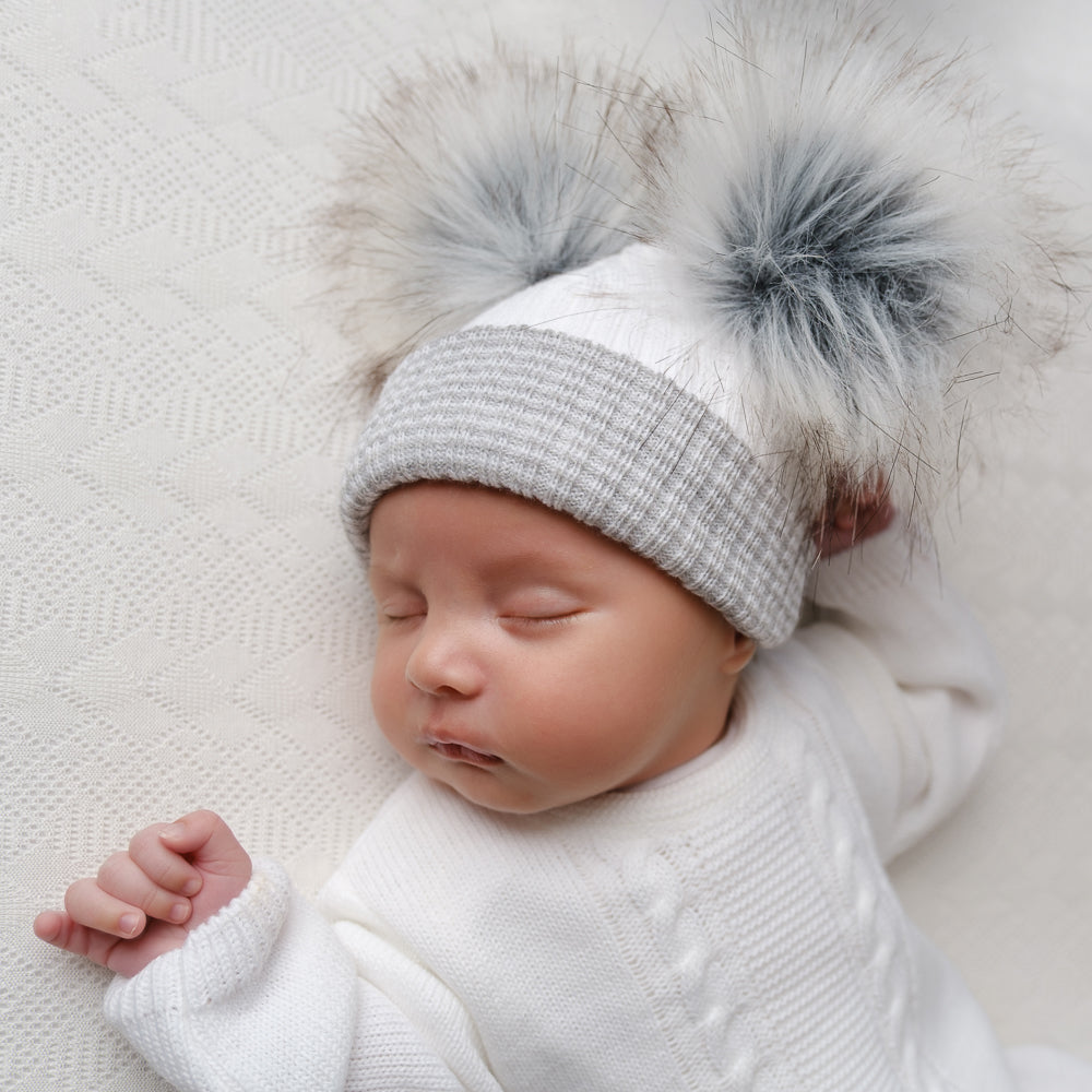 Sleeping baby wearing first size white and grey ribbed fur double pom hat