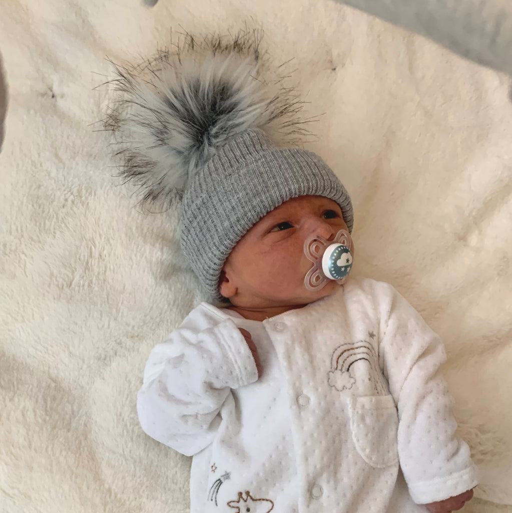 Baby wearing the first size grey ribbed fur pom hat