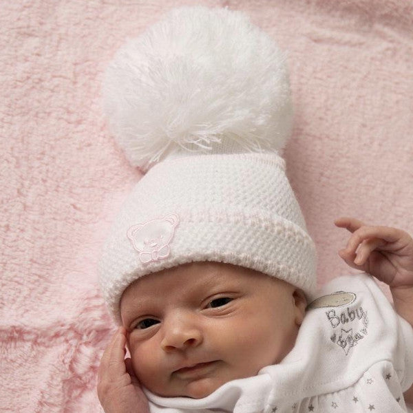 Baby wearing first size white/pink knitted stripe pom hat with teddy