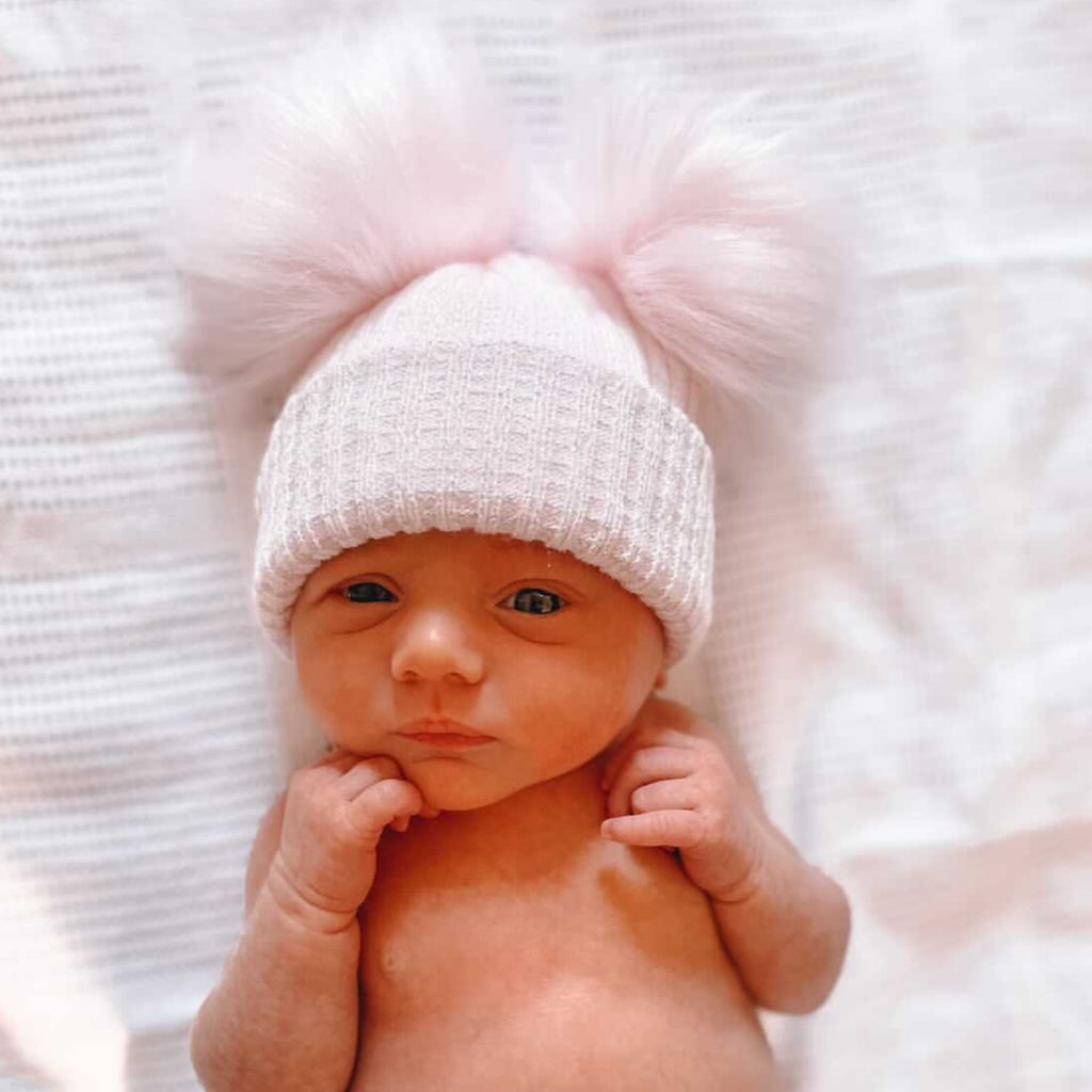 Baby wearing first size pink and silver ribbed fur double pom hat