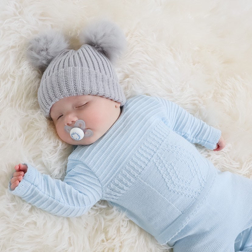 Sleeping baby with dummy and pom pom hat wearing blue diamond knitted set