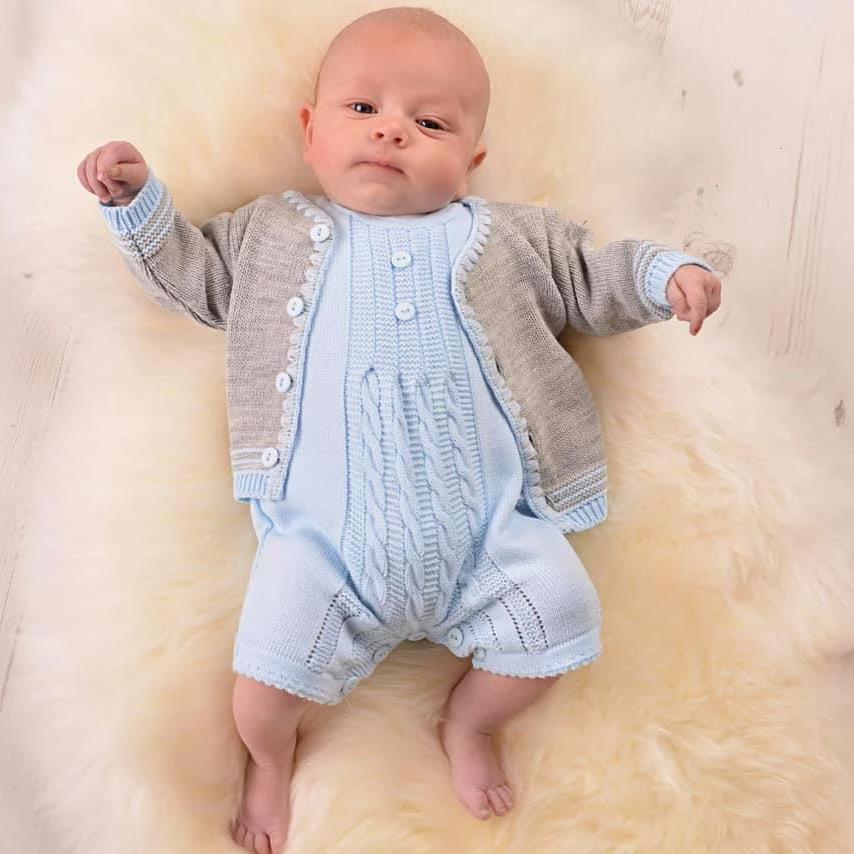 Baby wearing blue cable knitted romper and grey cardigan