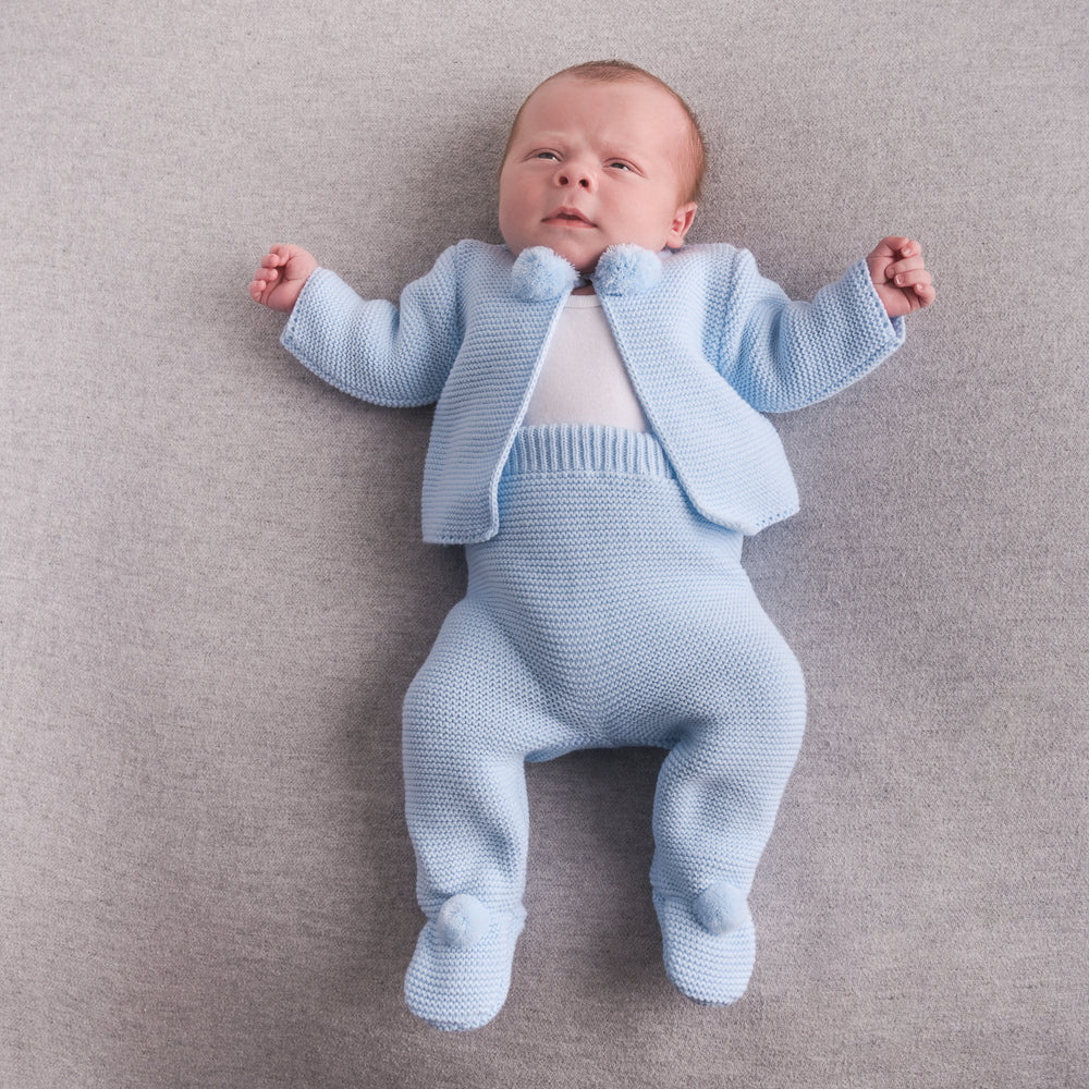 Baby on grey carpet wearing blue knitted pom outfit