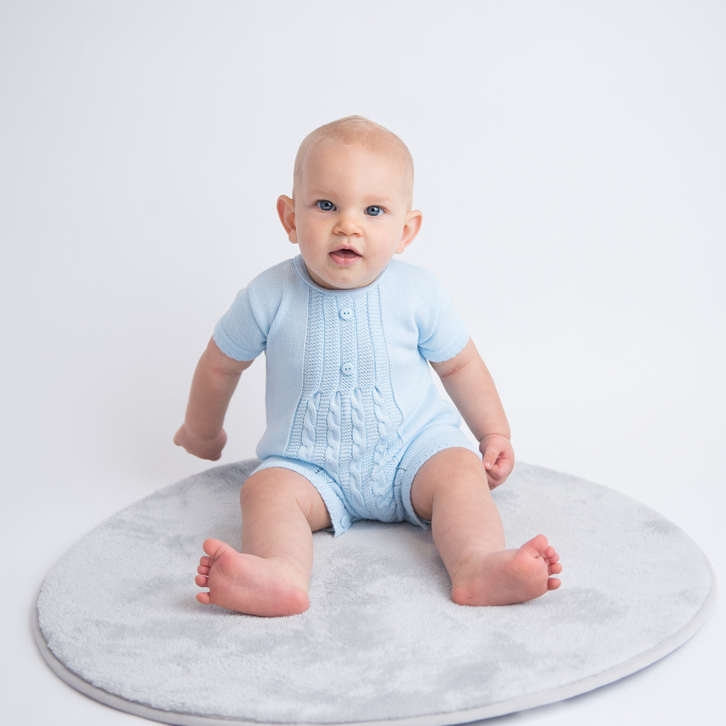 Baby sat on grey rug wearing blue cable knitted romper