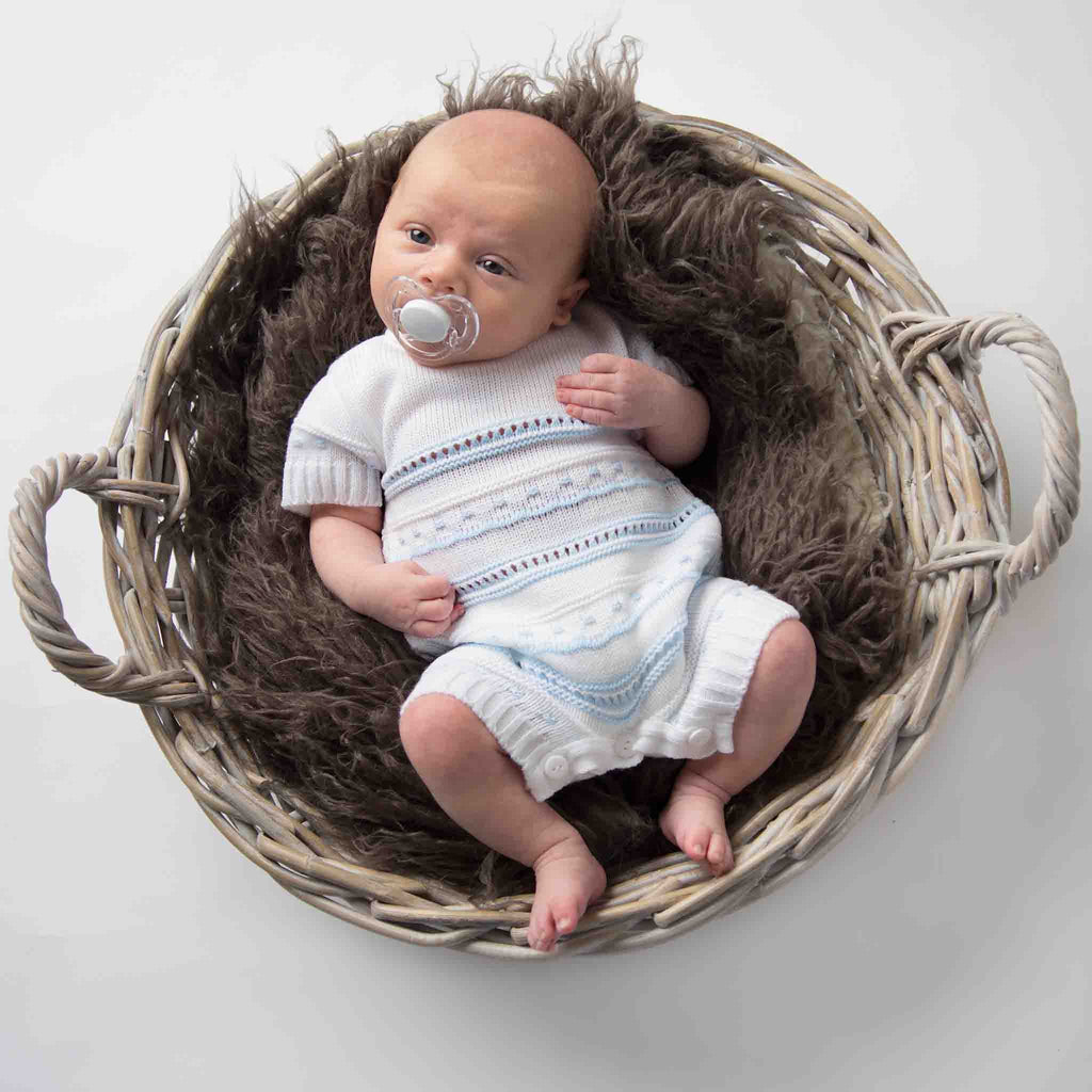 Baby in basket wearing blue and white knitted pointelle romper