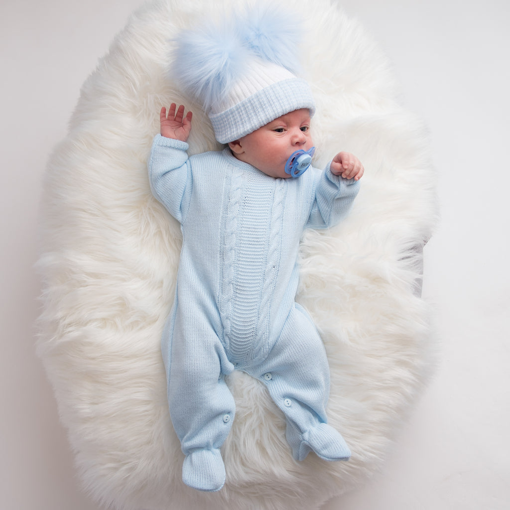 Baby on white fur blanket wearing blue cable knitted onesie