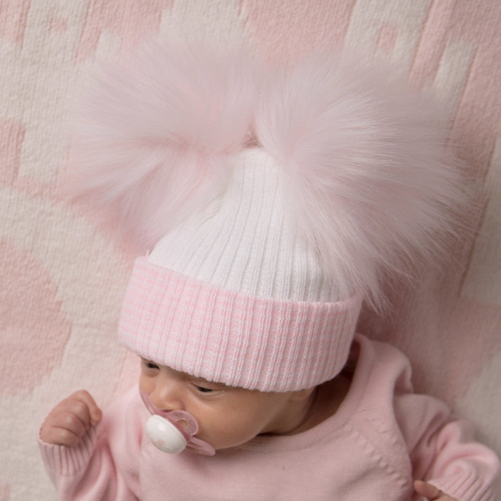Baby on pink blanket with dummy wearing the first size white and pink ribbed fur double pom hat