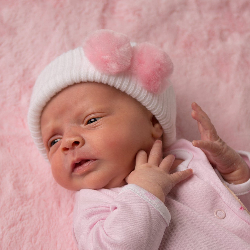 Baby wearing first size white hat with pink pom pom