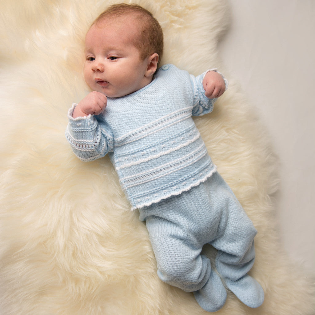 Baby laying on cream fur rug wearing blue and white pointelle knitted set