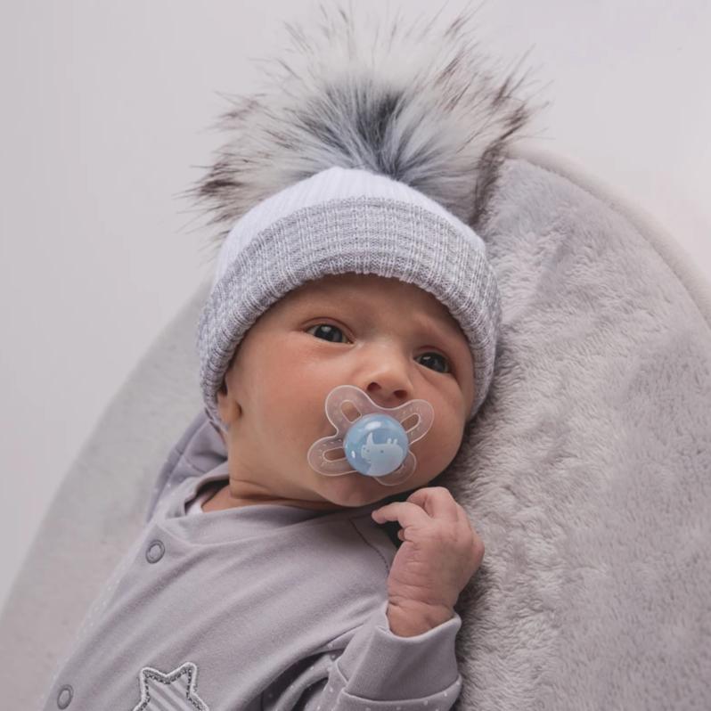 Baby with dummy wearing the first size white and grey ribbed fur pom hat