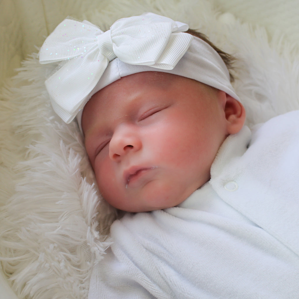 Baby wearing baby girl white bow headband with glitter detailing