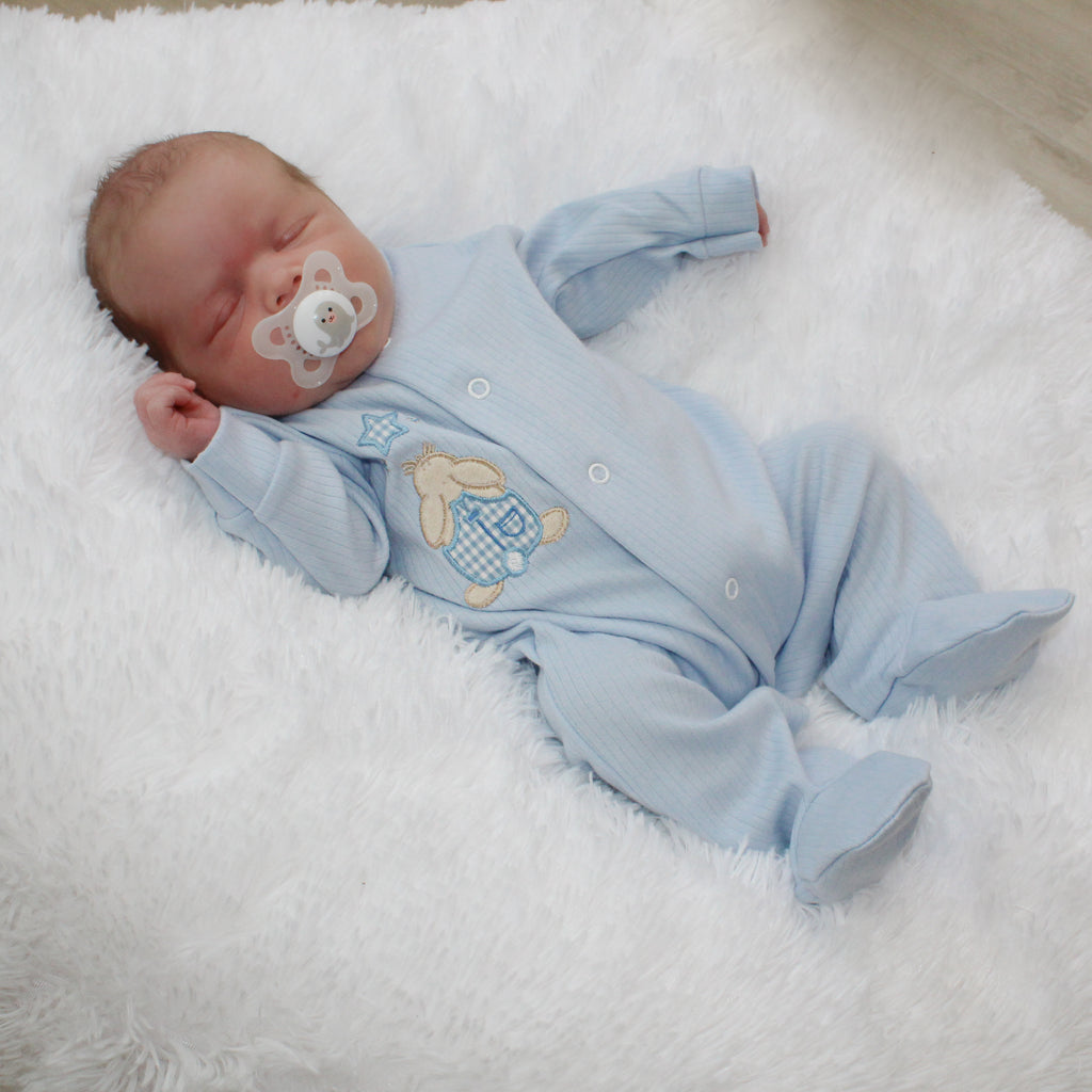 Sleeping baby with dummy on white fur blanket wearing the Blue Rabbit & Star Ribbed Sleepsuit