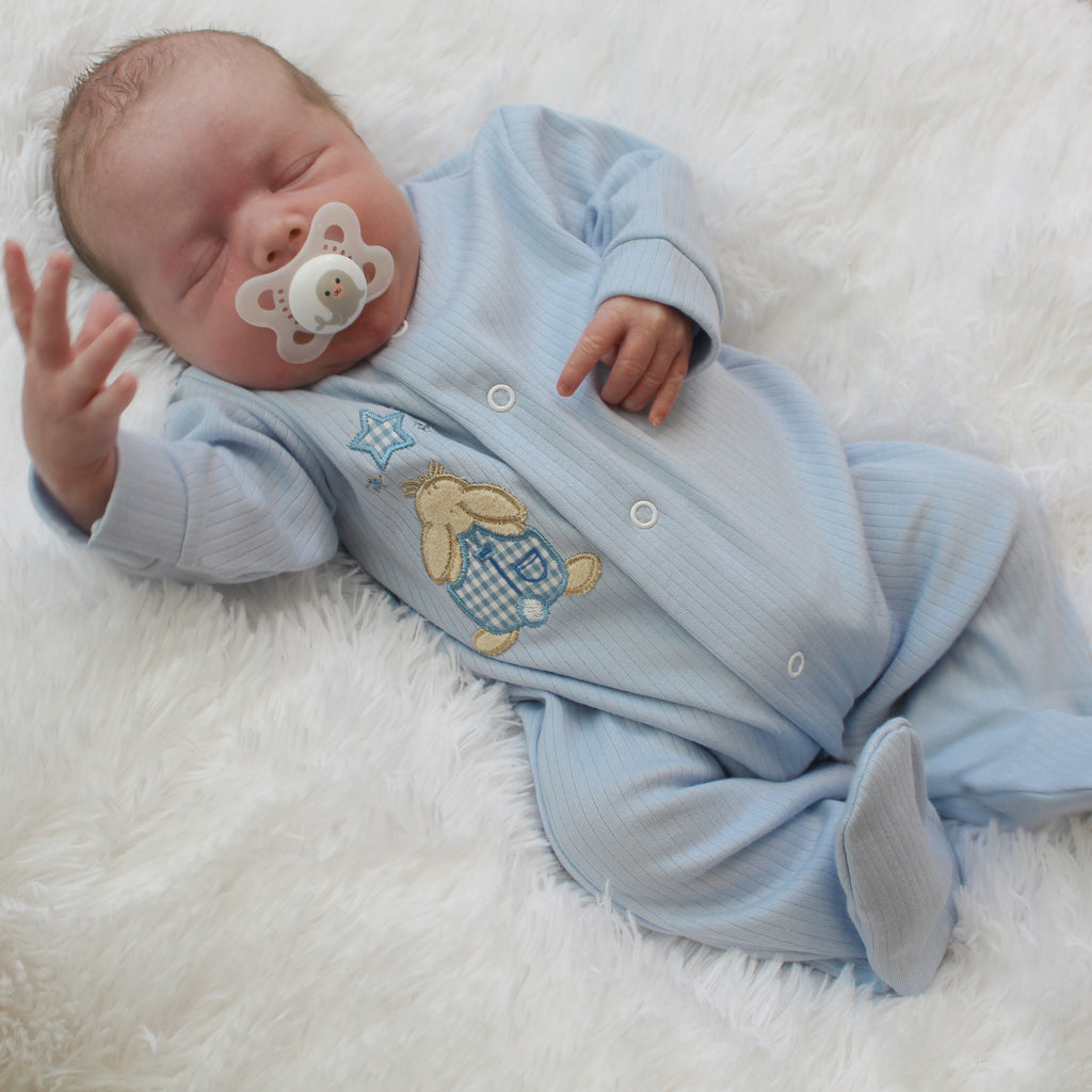Baby with hand in the air on white fur blanket wearing the blue rabbit and star ribbed sleepsuit