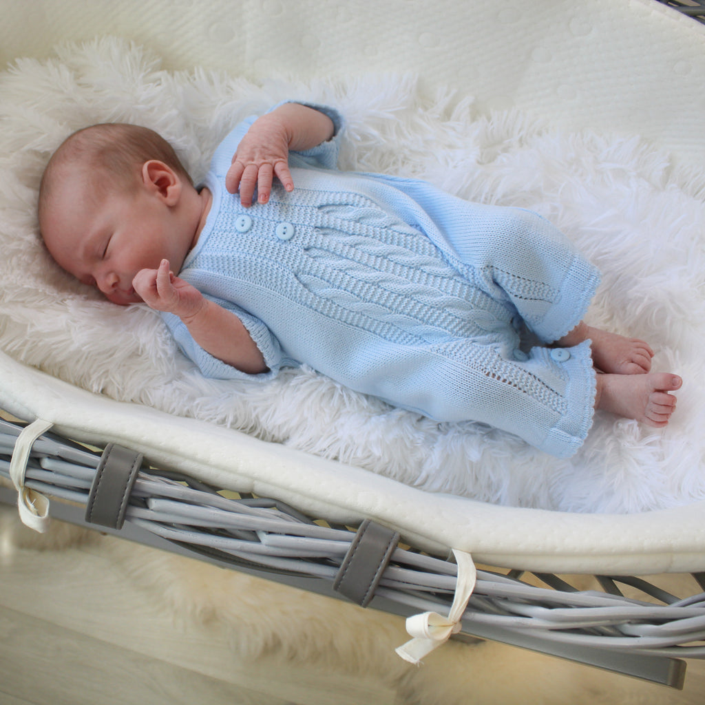 Baby in moses basket wearing blue cable knitted romper