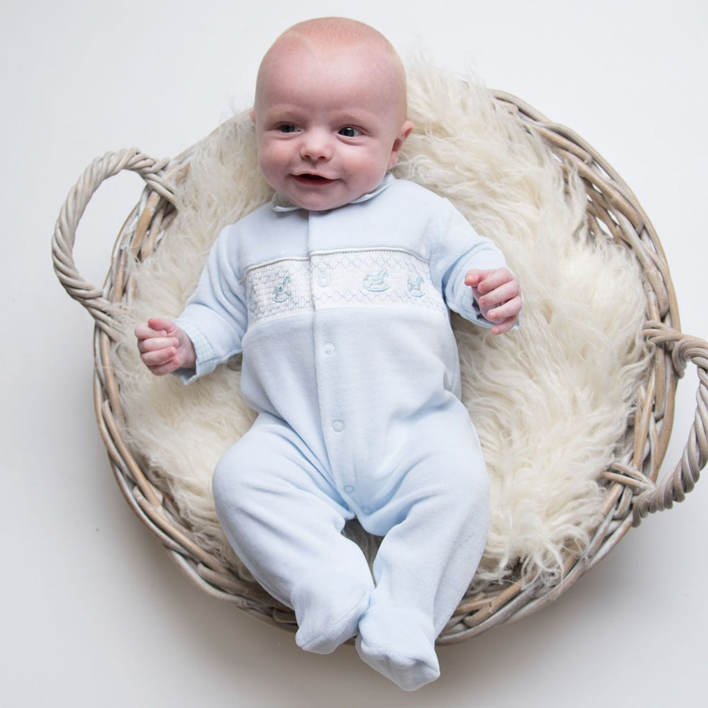 Baby in basket on cream fur blanket wearing baby boys rocking horse smocked velour sleepsuit