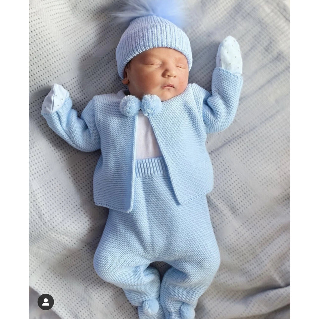 Baby with arms up and sleeping wearing the blue knitted pom outfit