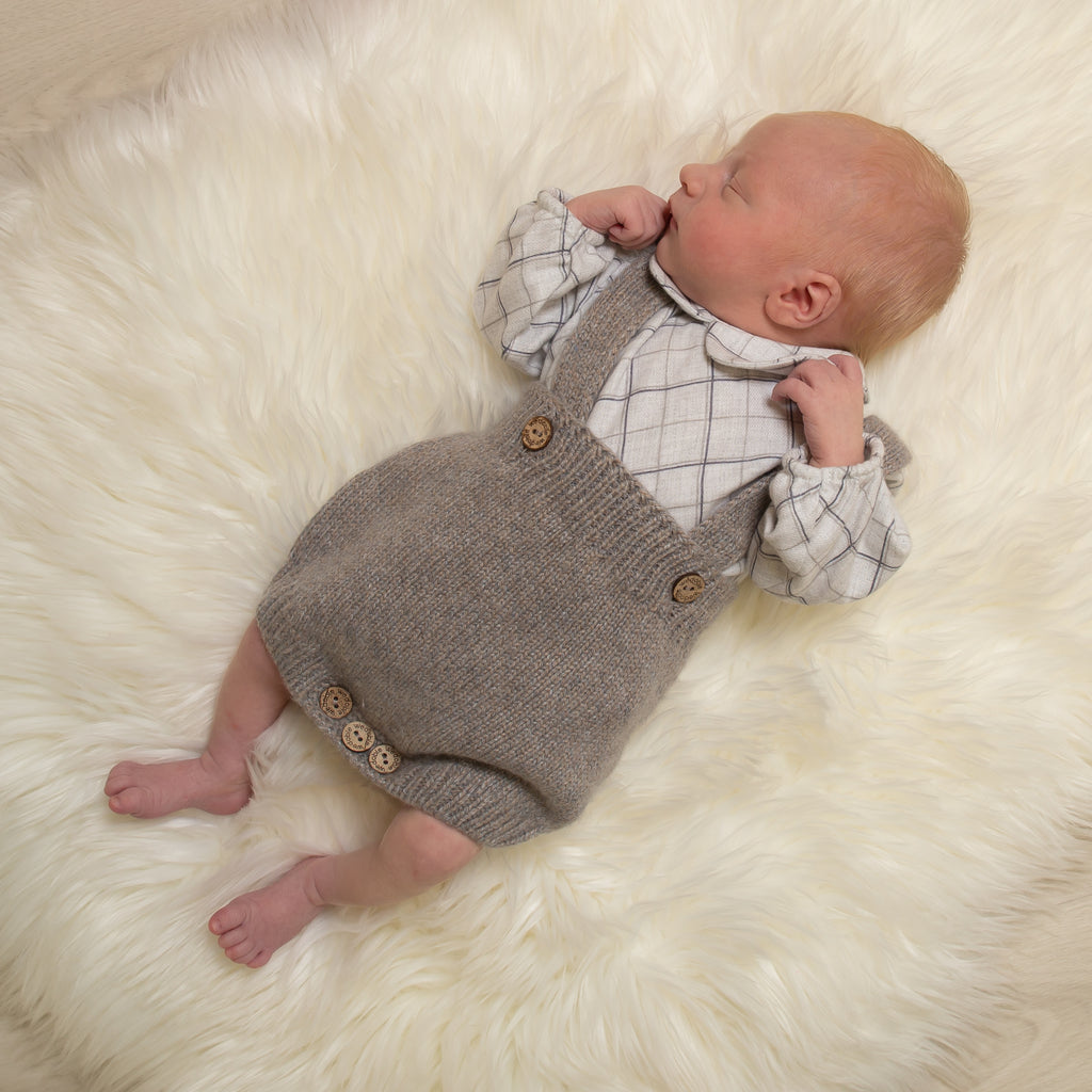 Baby laid on white fur blanket wearing check shirt bodysuit and knitted dungarees