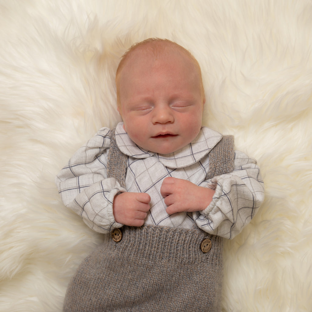 Sleeping baby on white fur background wearing check shirt bodysuit and knitted dungarees