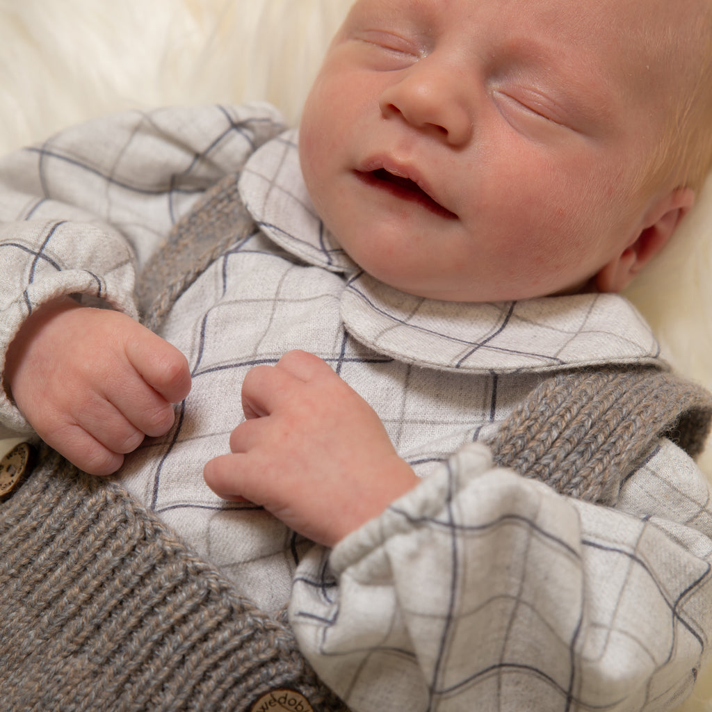 Close up of baby wearing check shirt bodysuit and knitted dungarees