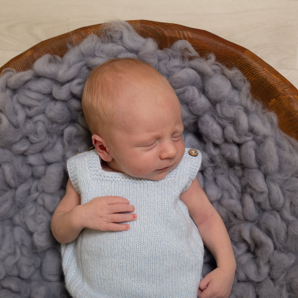 Sleeping baby on grey blanket in wooden bowl wearing Blue Wool Knit Dungarees