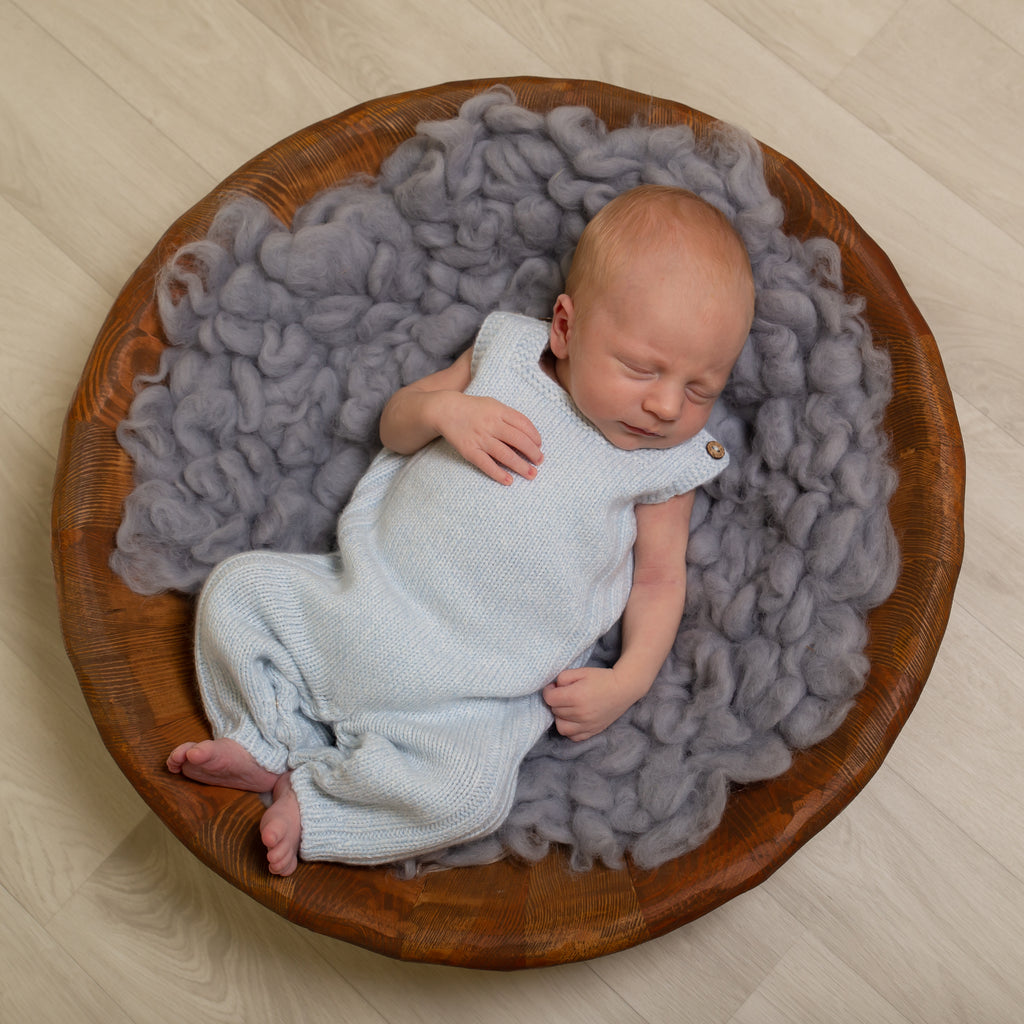 Baby asleep in wooden bowl on grey wool wearing the blue wool knit dunagrees