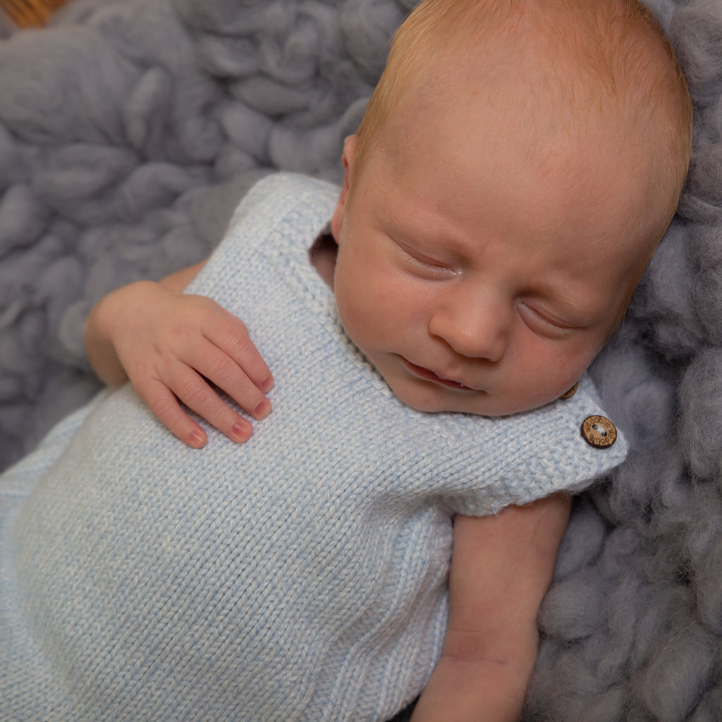 Close up of sleeping baby wearing blue wool knit dungarees