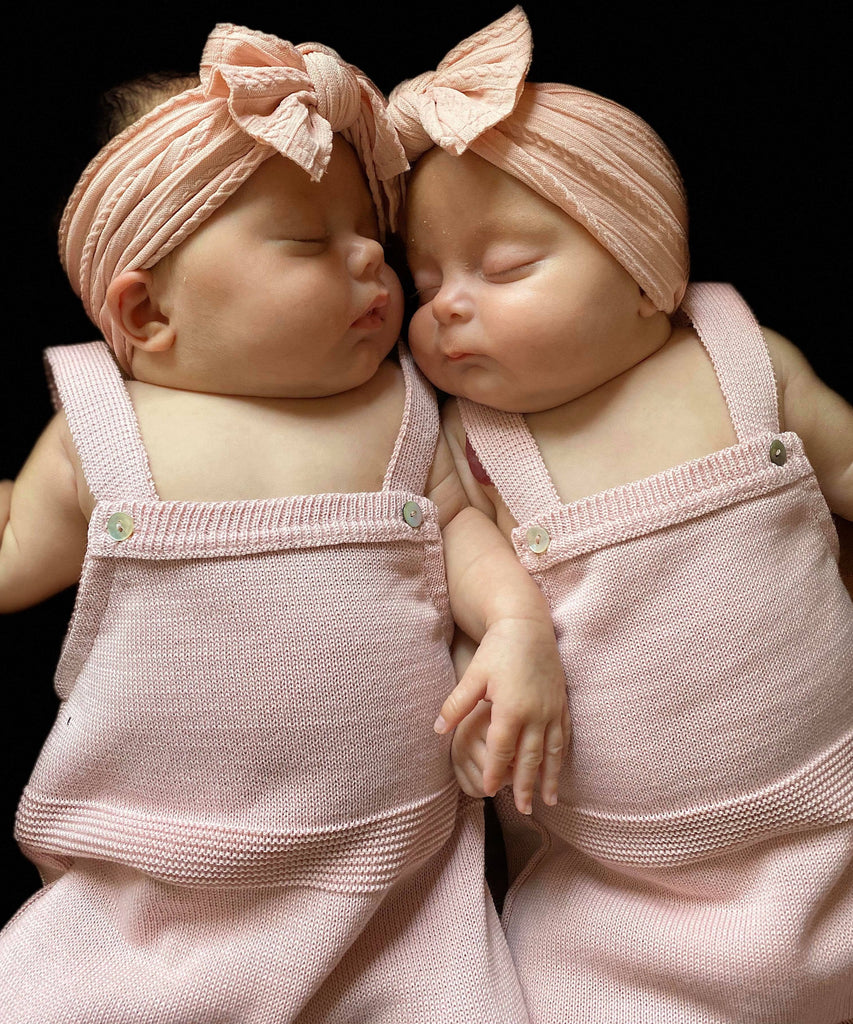 Two babies cuddling, both wearing the dusty pink knitted rompers