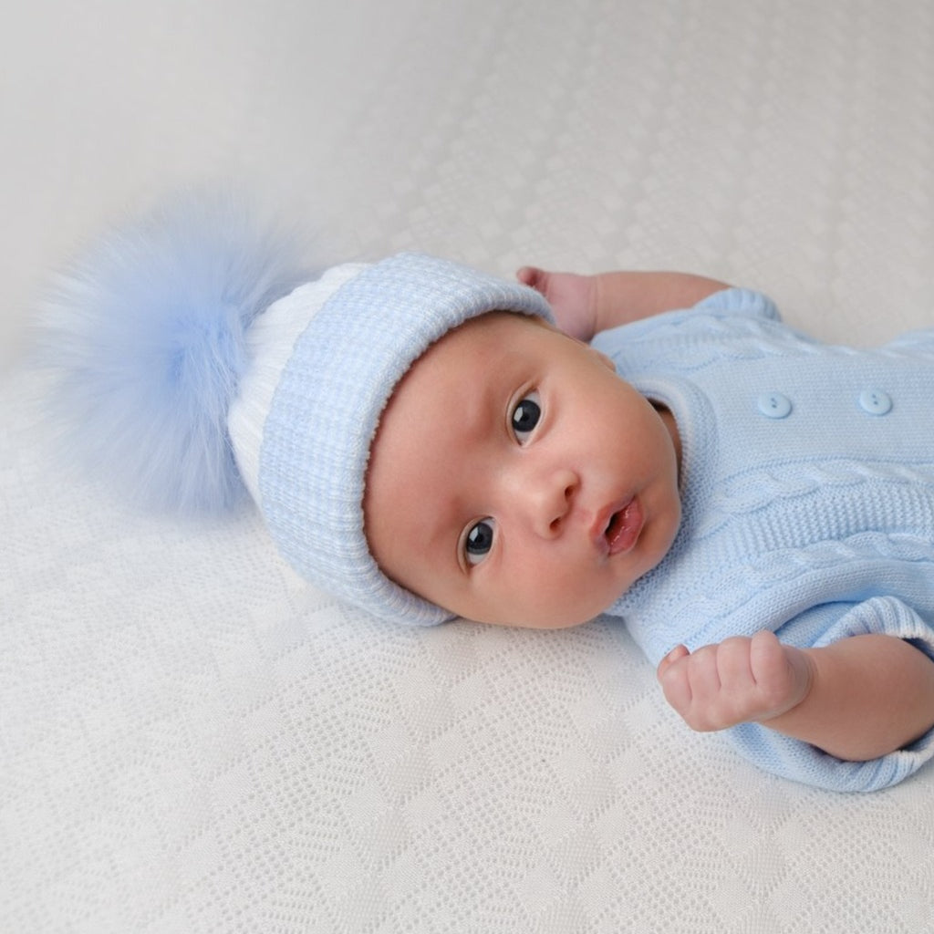 Close up of pouting baby wearing first size blue and white ribbed fur pom hat