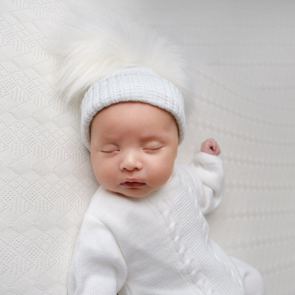 Sleeping baby wearing the first size white and silver ribbed fur pom hat