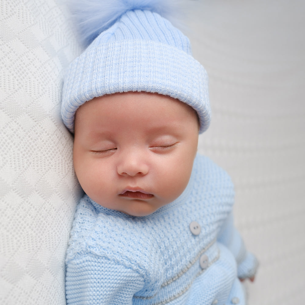 Sleeping baby wearing first size blue ribbed fur pom hat