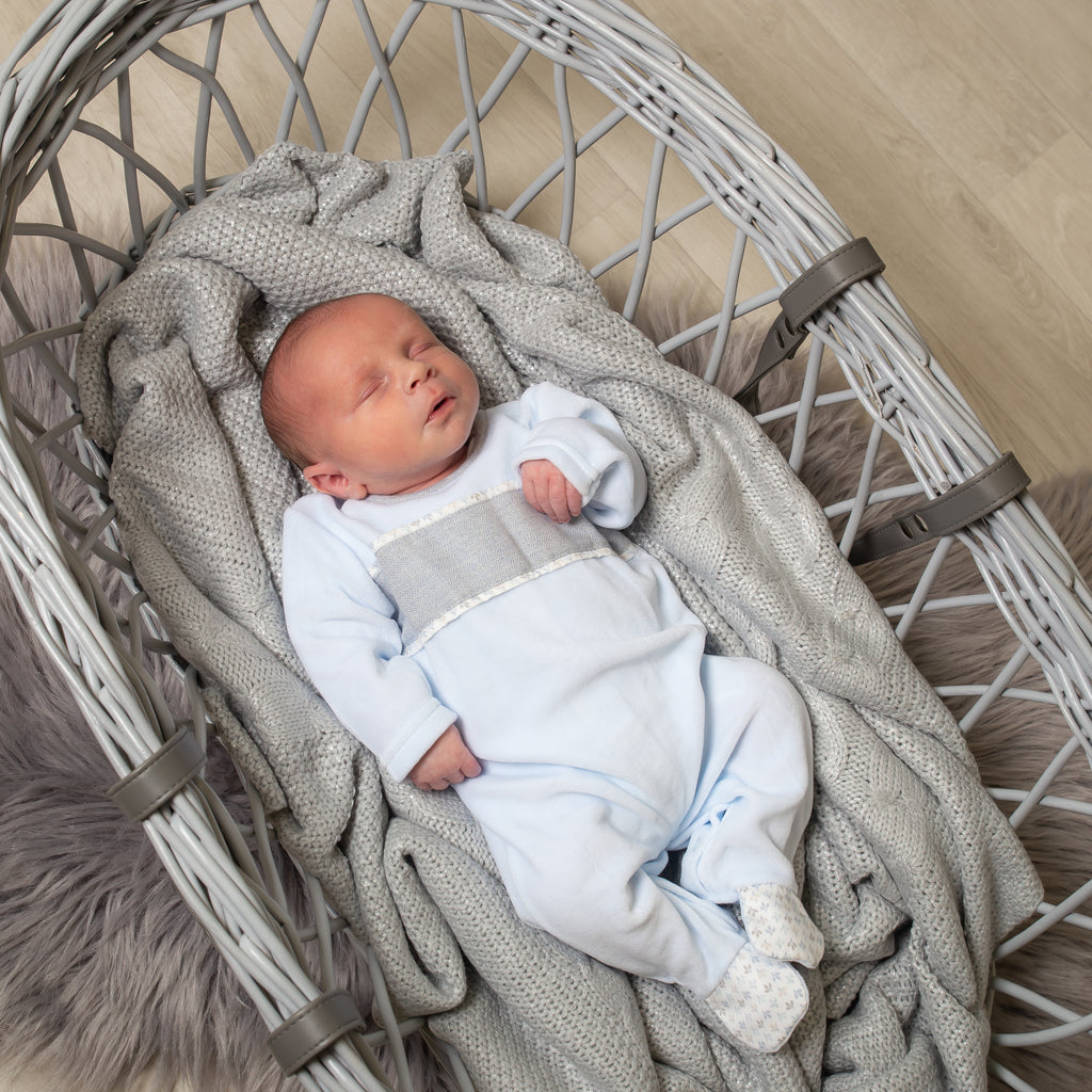 Sleeping baby in moses basket wearing the blue velour leaf print panel all in one