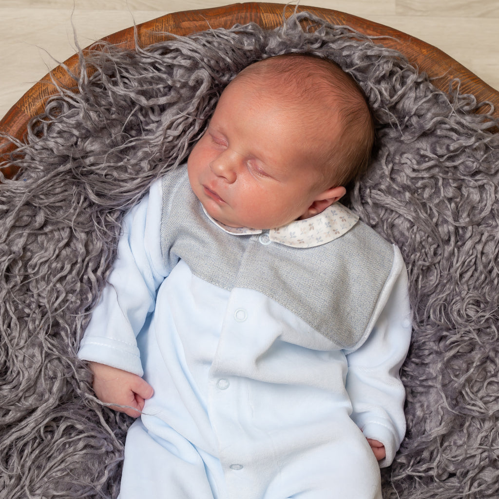 Sleeping baby in wooden bowl laid on a grey fur blanket wearing the Blue Velour Tweed Panel Leaf Sleepsuit