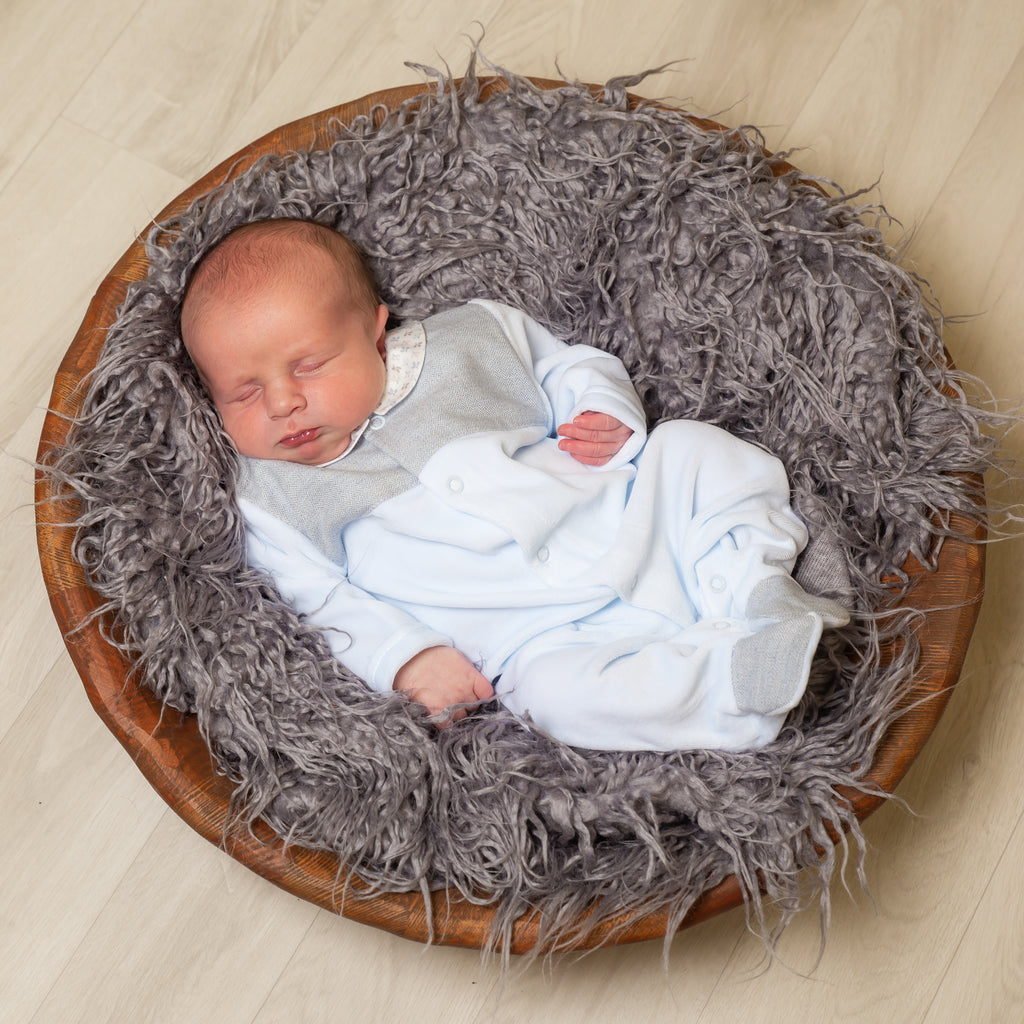 Baby in wooden bowl with grey fur blanket wearing the blue velour tweed panel leaf sleepuit