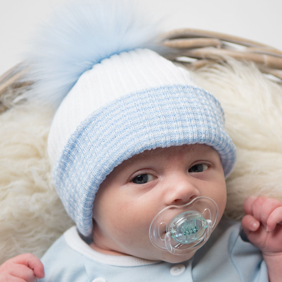 Baby with dummy wearing the first size blue and white ribbed fur pom hat