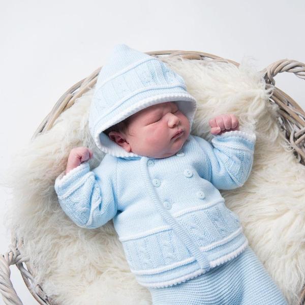 Baby on fur blanket in basket wearing blue and white knitted jacket with hood up