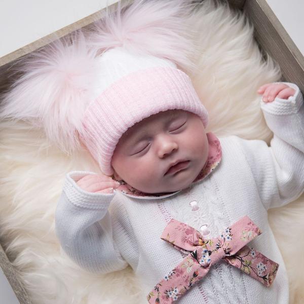 Sleeping baby wearing first size white and pink ribbed fur double pom hat