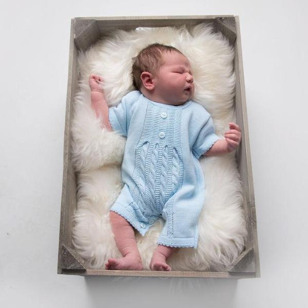 Baby in wooden box wearing blue cable knitted romper