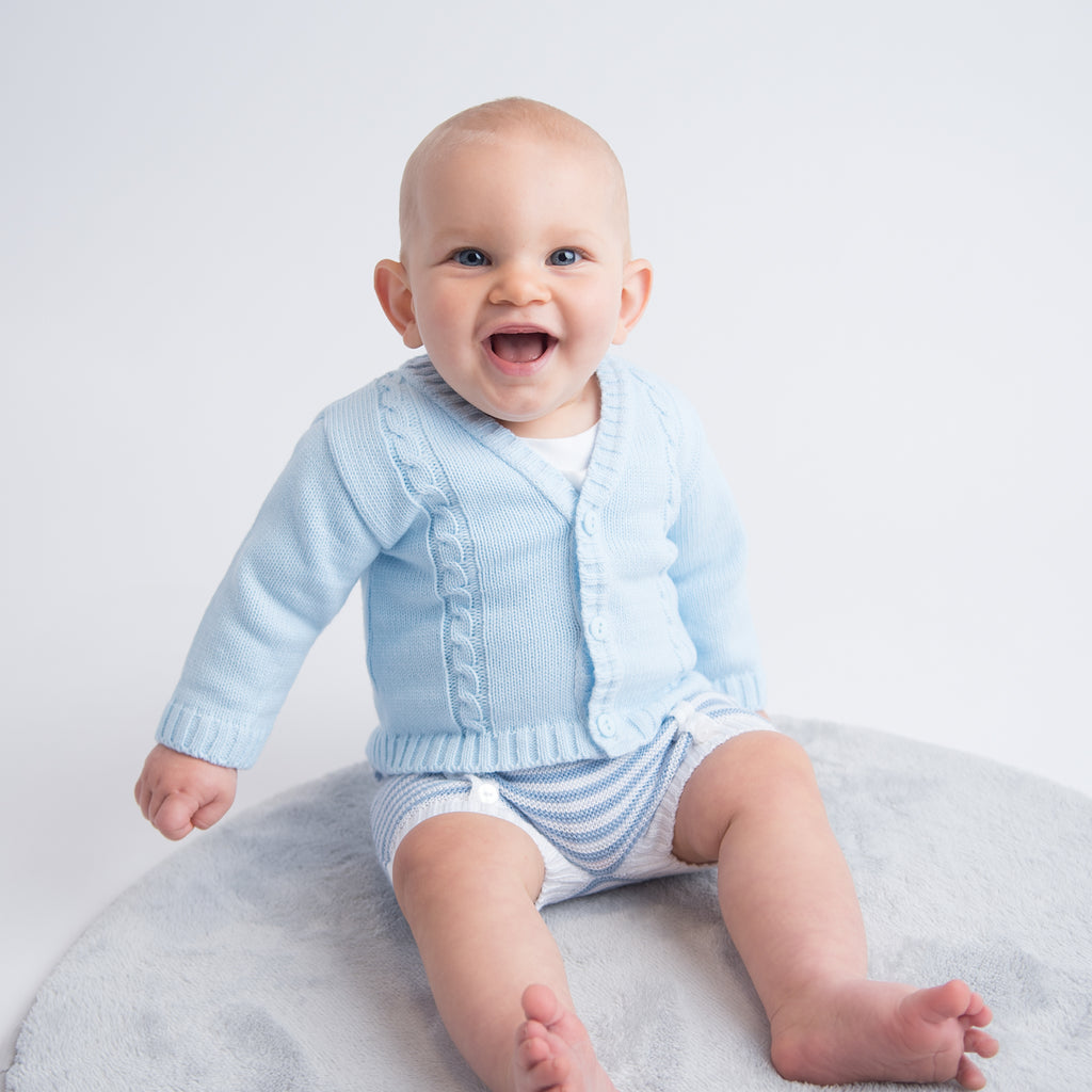 Baby sat up wearing a blue cable knitted cardigan