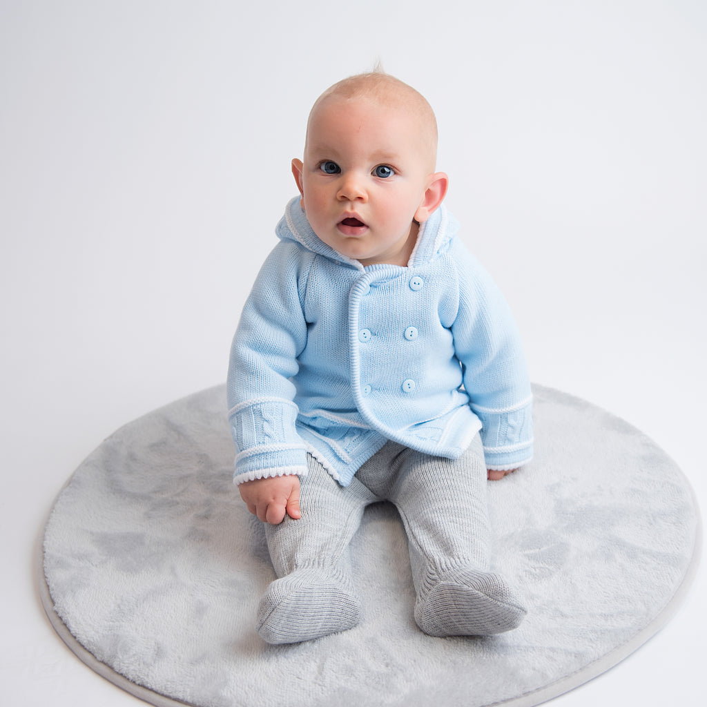 Baby on grey circle fur rug wearing buttoned up blue & white knitted jacket