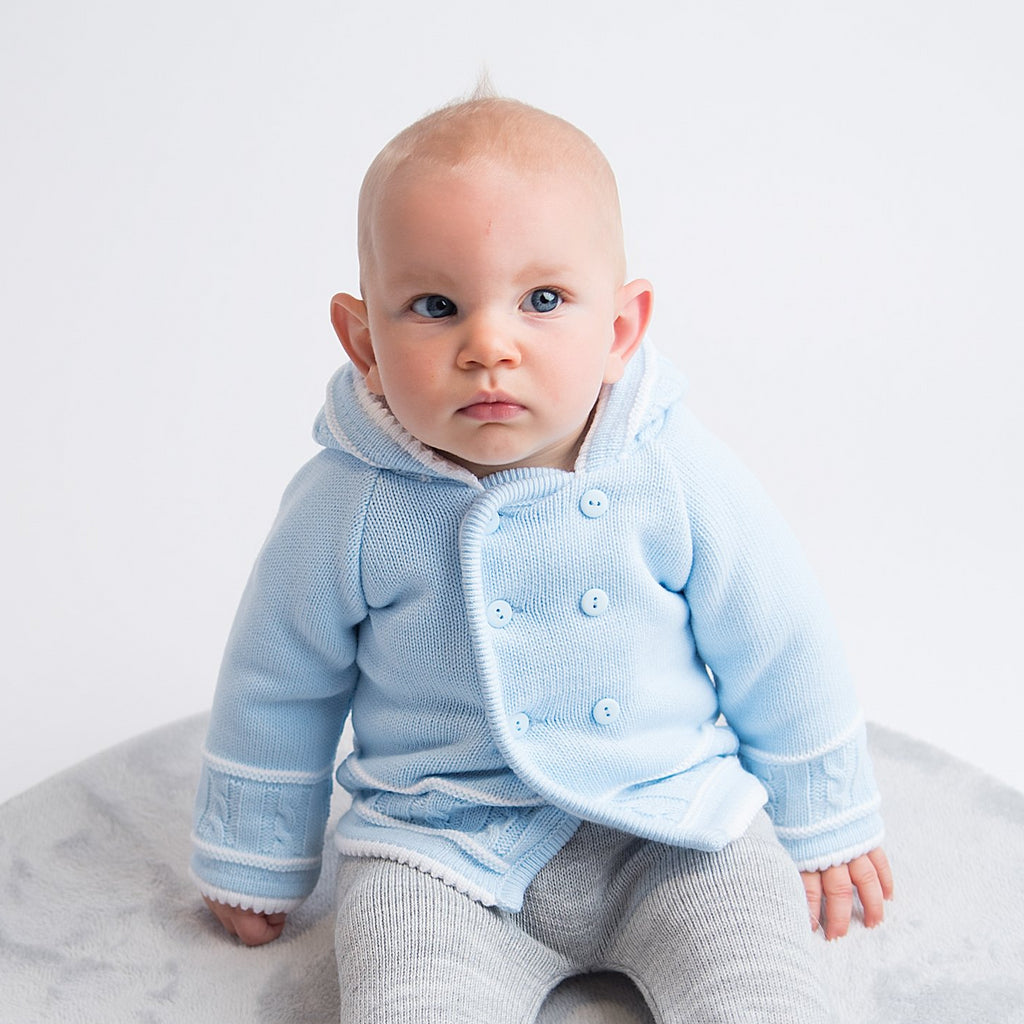 Baby sat on fur rug wearing blue and white knitted jacket