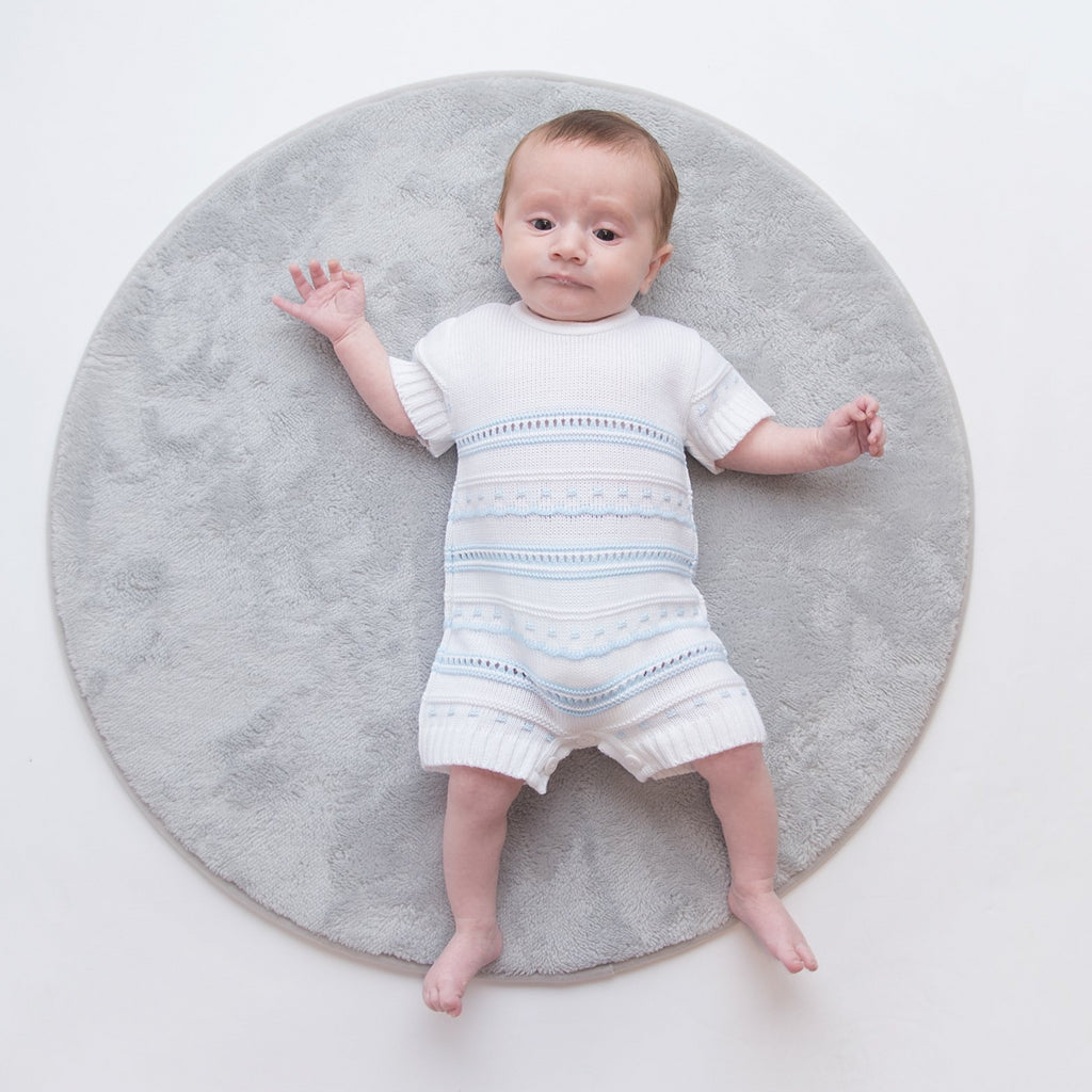 Baby on grey fur rug wearing blue and white knitted pointelle romper