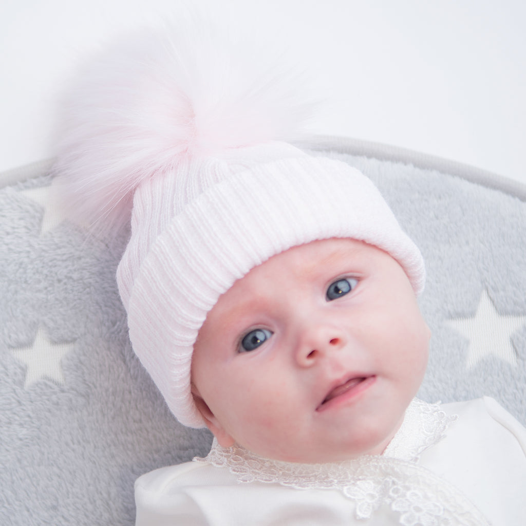 Baby on grey star rug wearing the first size pink ribbed fur pom hat