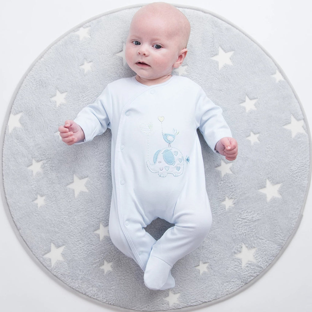 Baby wearing 'Elephant & Bird' blue cotton sleepsuit on mat 