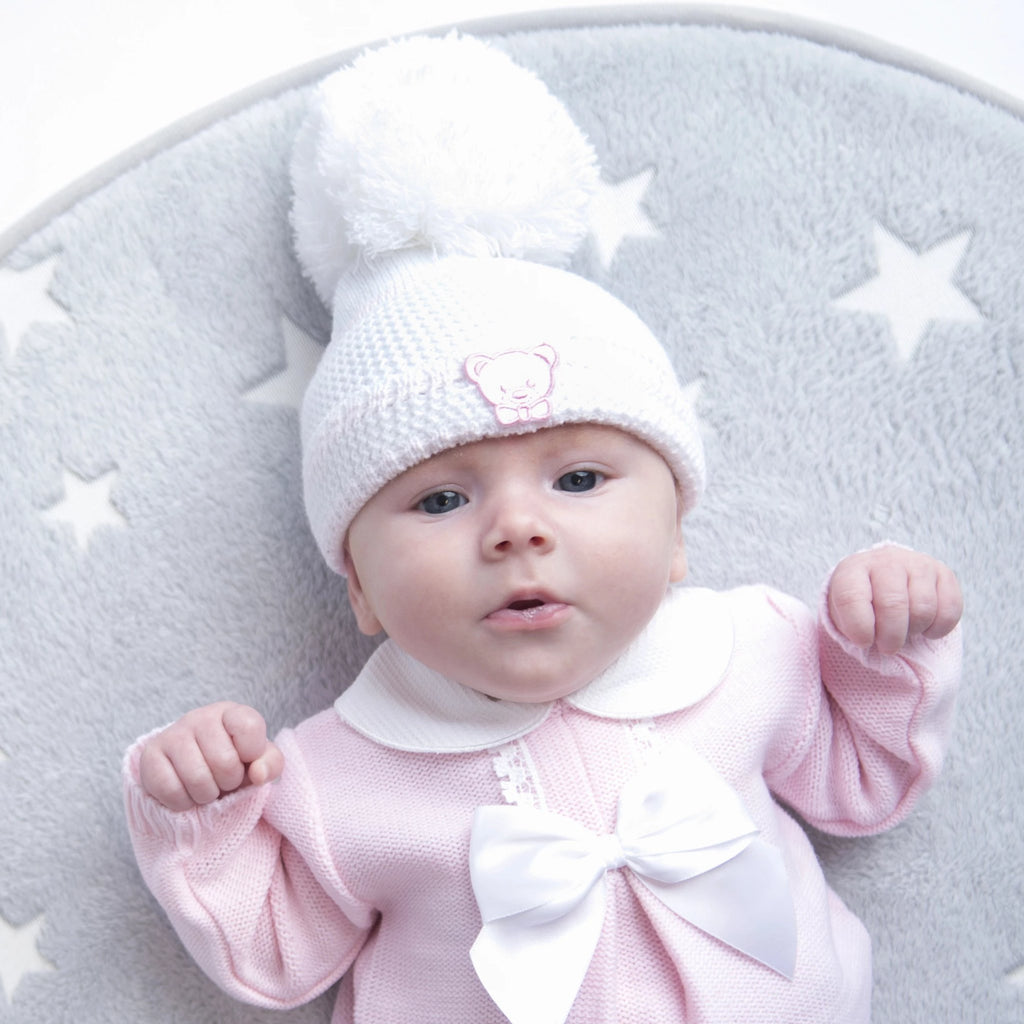Baby on grey star rug wearing the first size white/pink knitted stripe pom hat with teddy